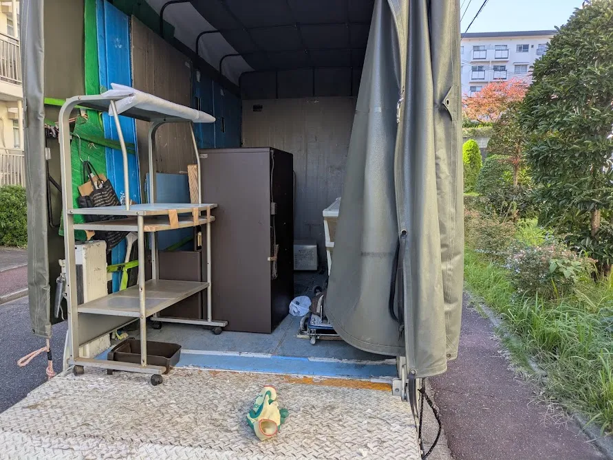 堺市南区原山台で回収したパソコンラック・レンジ台・プラスチックケースなどの不用品をトラック荷台に載せている作業中の写真